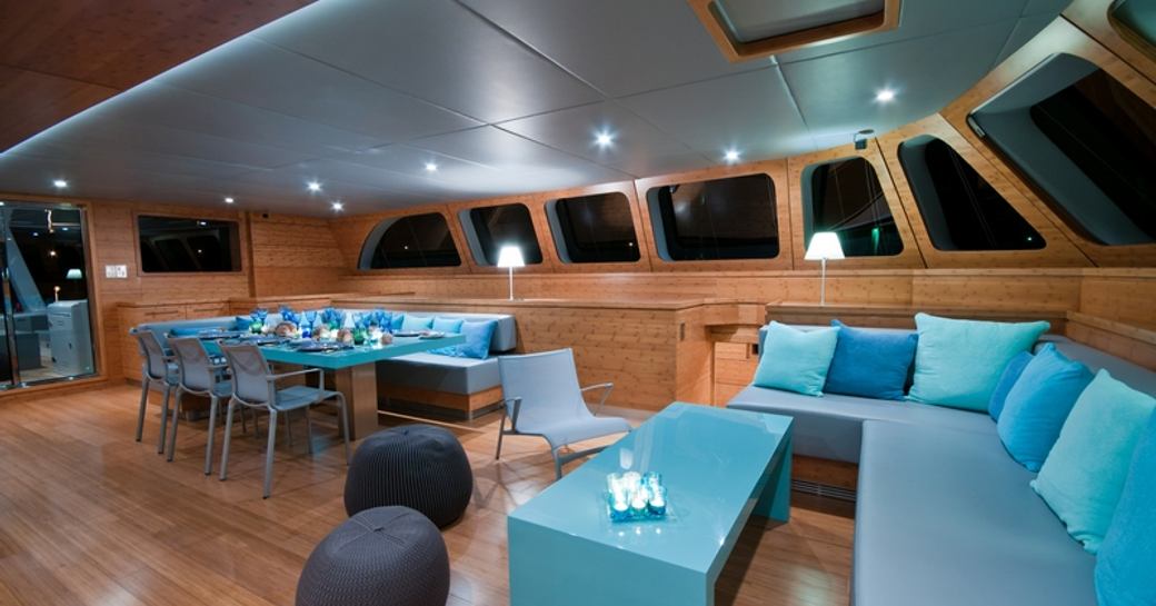 the main salon with adjoining dining area inside superyacht che designed with wood embellishments and turquoise accents 