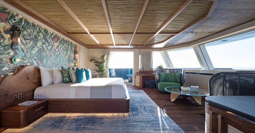 Master cabin onboard charter yacht KING BENJI, central berth with armchair and coffee table opposite, with wide reaching windows around the front of the cabin