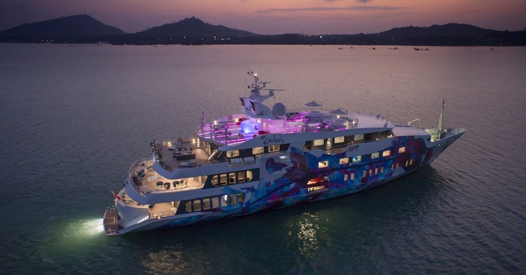 A colorfully decorated superyacht cruises at night with its lights on