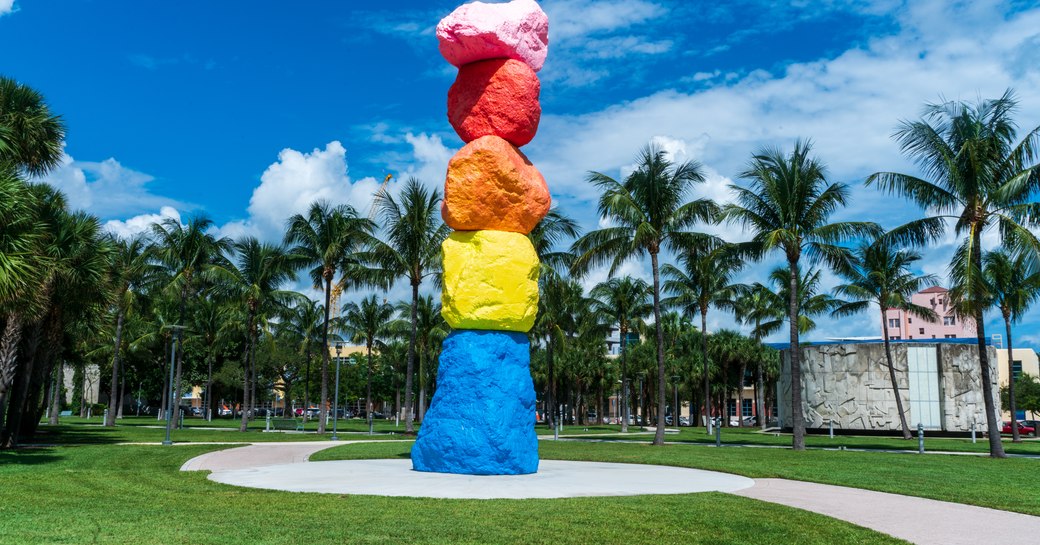 Rainbow sculpture on display at Art Basel Miami, surrounded by grass and palms