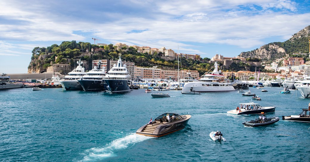 Port Hercule, Monaco at sea level. Motor yachts moored in marina with a tender sailing in.