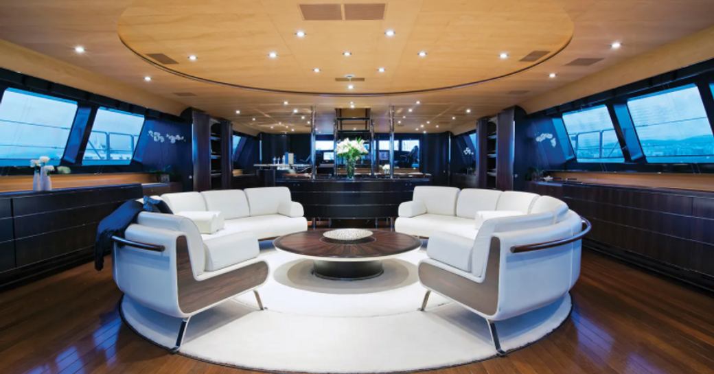 Main salon onboard Parsifal III, central curved sofas facing each other around a coffee table with windows across both sides