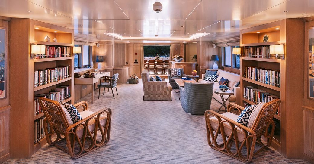 Overview of the main salon onboard charter yacht NATALIA V, lounge area in the background with bookshelves and a pair of armchairs forward