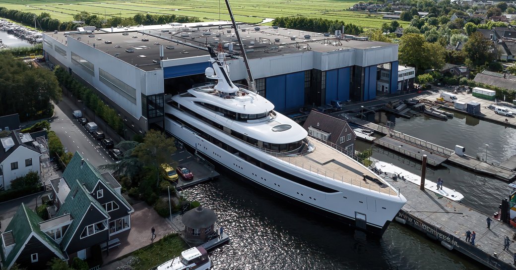 Feadship 'Project 822' emerges from her construction shed for the first time, with lush green fields in the background.