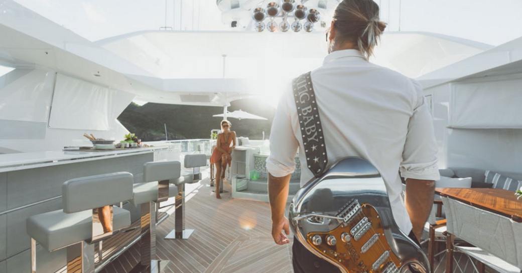man with guitar walks down sundeck towards woman seated at swim-up bar on board superyacht King Baby 