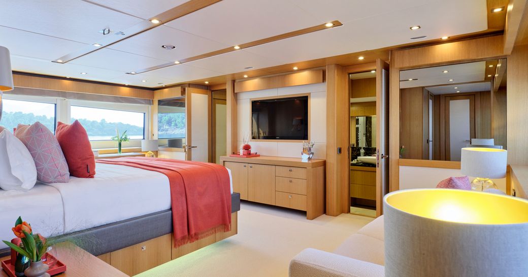 Overview of the master cabin onboard charter yacht MAKANI II, central berth facing a wall-mounted TV with large windows in the background