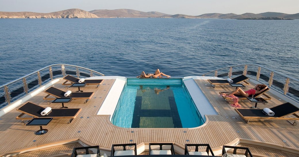 Charter guests sunbathing beside swimming pool on main deck of luxury yacht Alfa Nero 