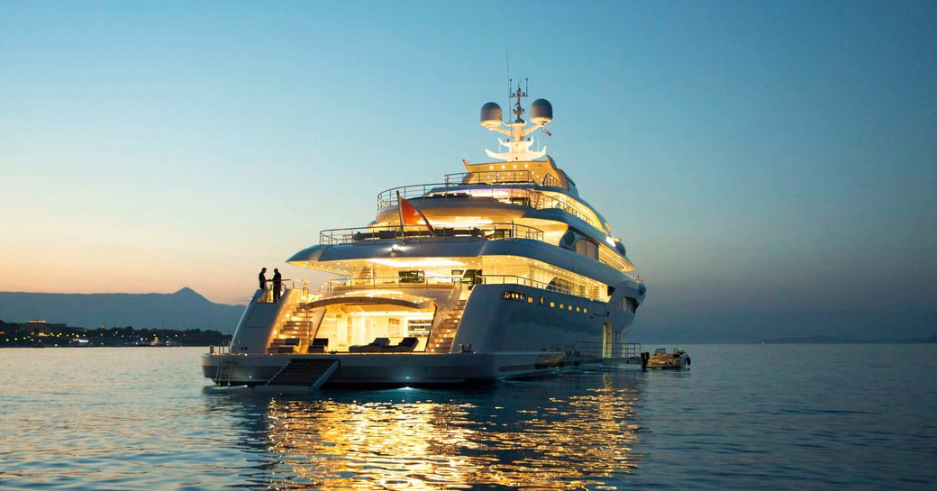 aft of superyacht O’PTASIA lit up at dusk while on a charter vacation