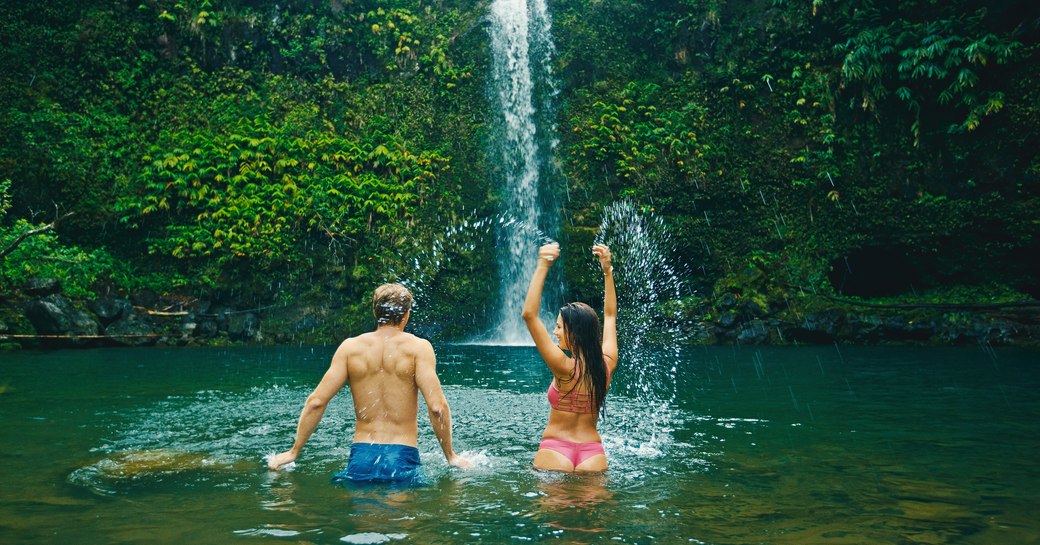 The back of a man who stands close to a cascading waterfall with a woman to his right