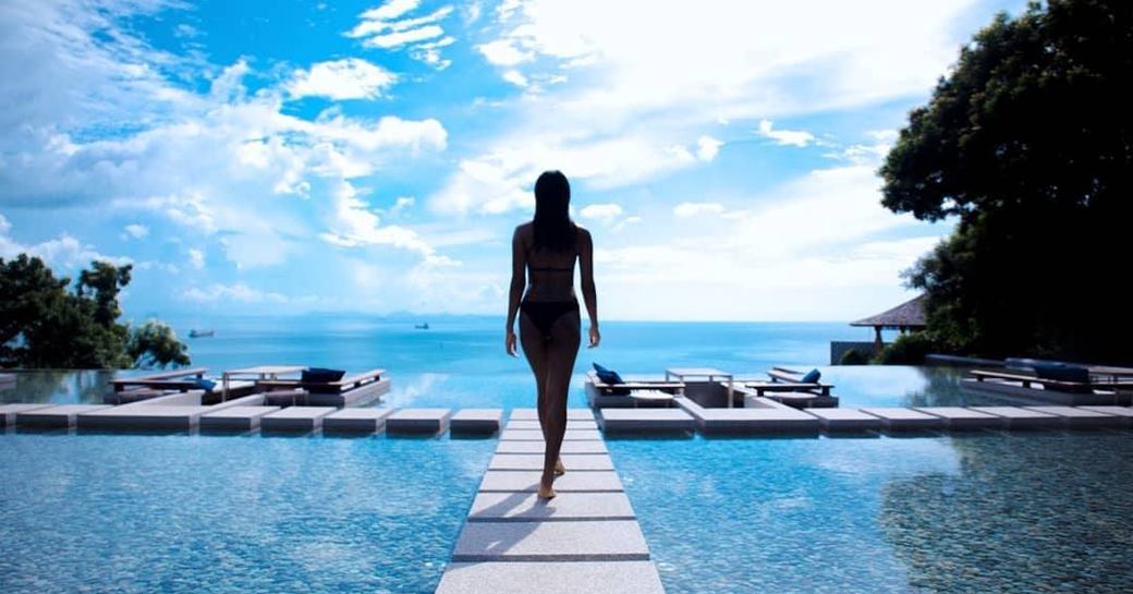 A woman walks across a wooden pontoon along an infinity pool at a resort in Phuket, Thailand