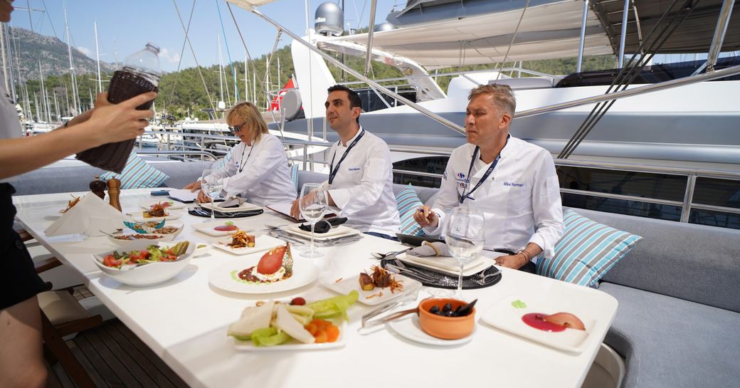 Three judges at the TYBA Charter Yacht Show Chef Competition with a spread of competition entries on a table