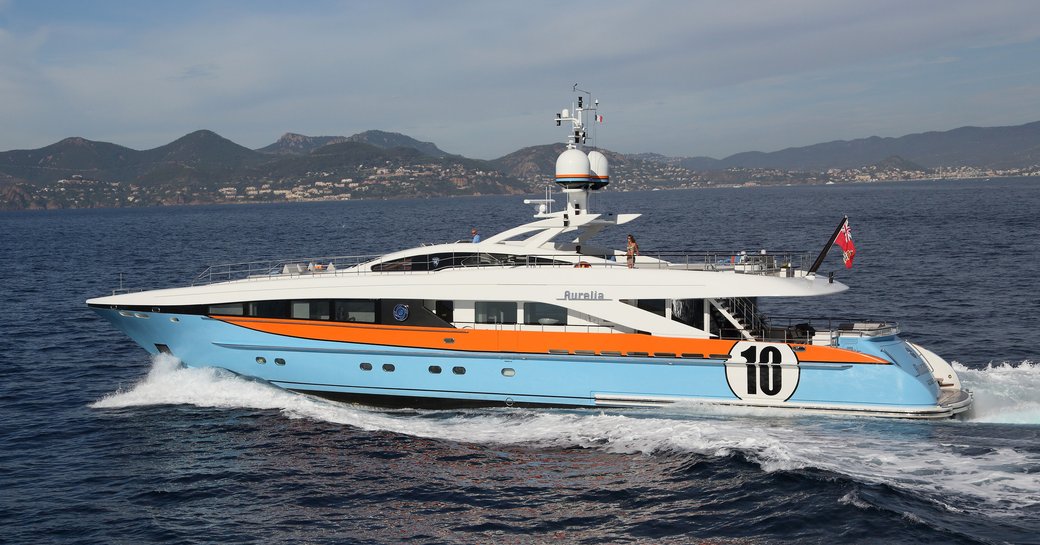 Woman stands on deck of superyacht AURELIA as she cuts through the water showing off her racecar-inspired profile in shades of blue and orange