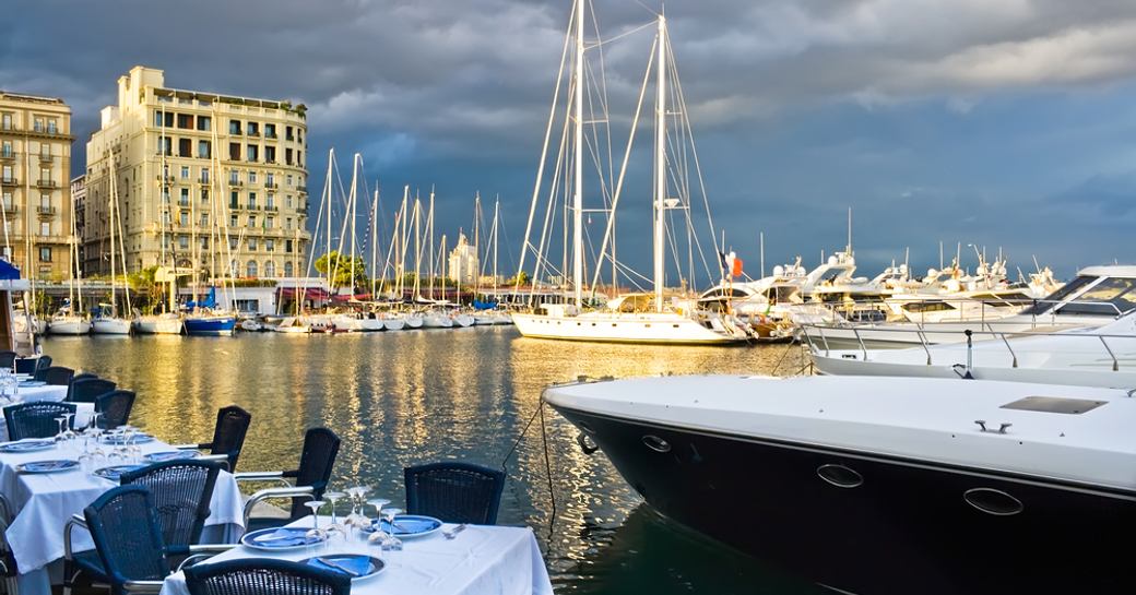 Sailing yachts in a Naples harbor against a stormy sky with dining tables in the foreground
