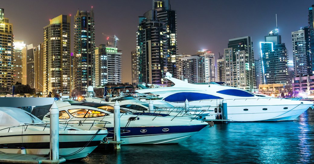 Yachts lined up in Dubai Harbour at night with cityscape in background