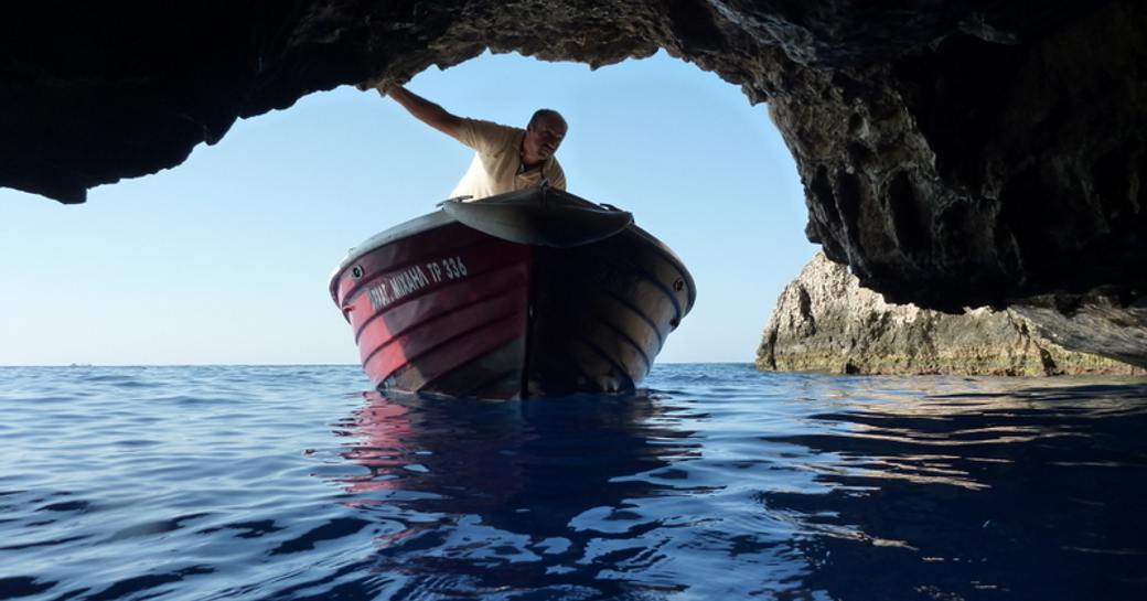 A man in a small boat navigating the low cave entrance to the Blue grotto in Greece
