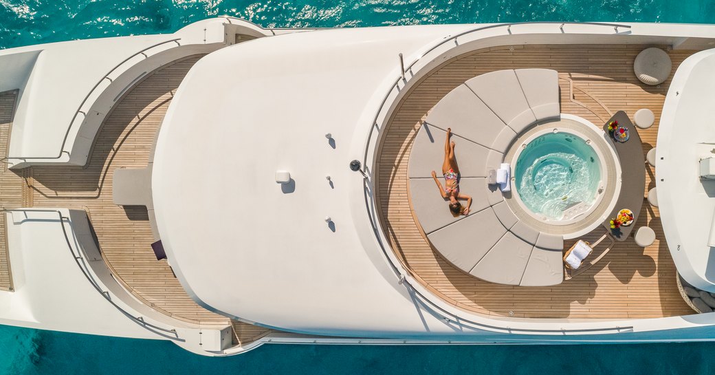 Elevated view looking directly down on the exterior decks onboard charter yacht BIG SKY, with a deck Jacuzzi and a charter guest relaxing on adjacent sun pads