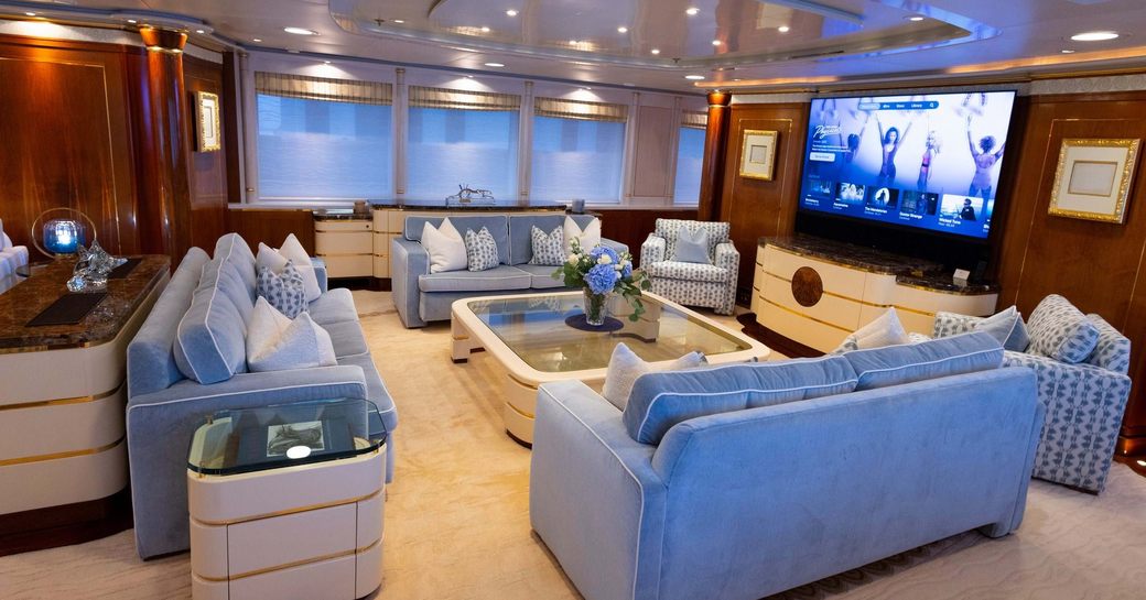 Overview of the lounge onboard charter yacht OLYMPUS, plush seating facing in around a coffee table with a large, wall-mounted TV in front
