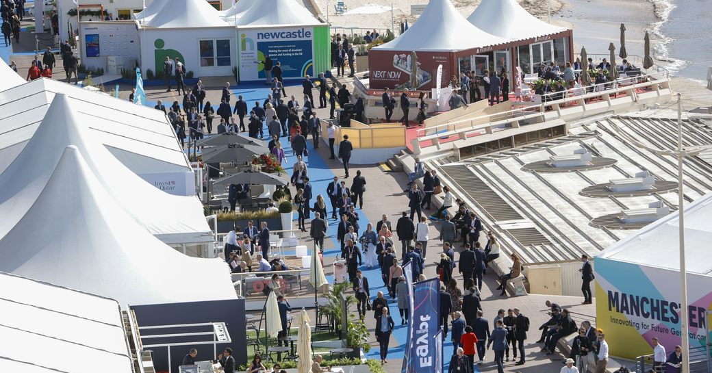 Elevated view looking down on MIPIM visitors walking along a blue carpet between exhibitor stands outside Palais des Festivals