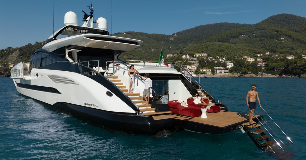 Aft view of charter yacht N1 at anchor with charter guests enjoying swim platform