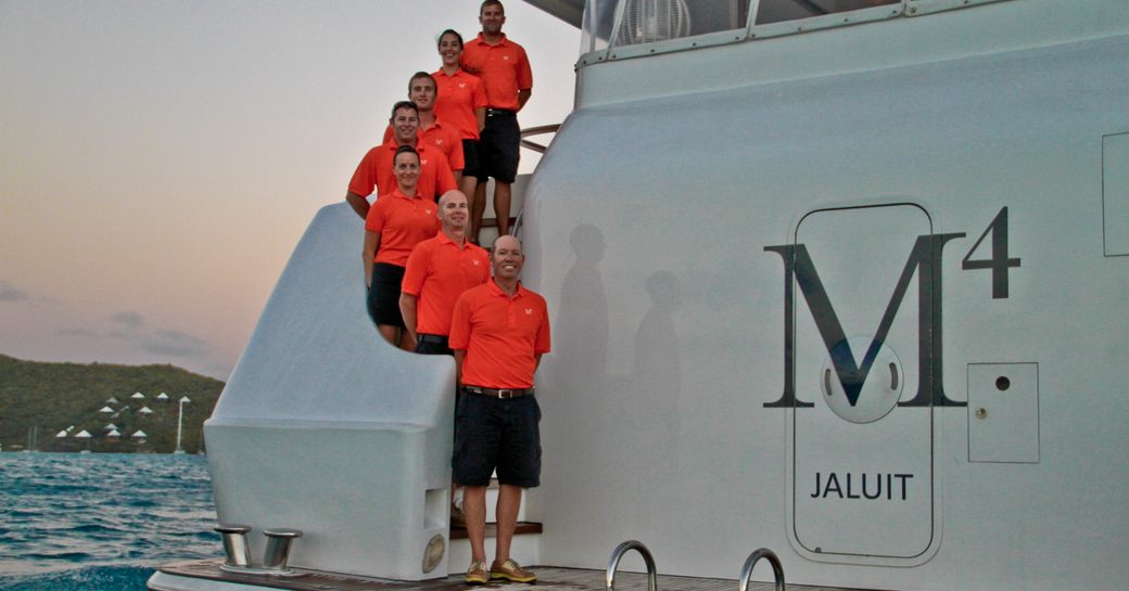 The crew on luxury yacht M4 stand near the sea platform in their orange uniforms.