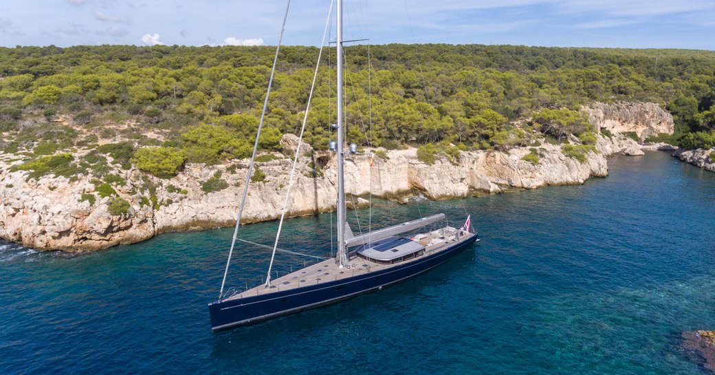 Aerial shot of superyacht G2 on the water, with Mediterranean landscape in background