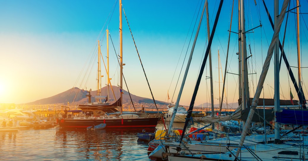 Sailing yachts in Naples, Italy with Mount Vesuvius in the distance against a setting sun