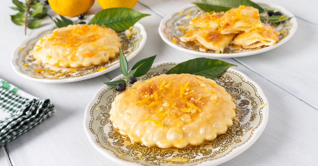 Three small plates each holding a Sardinian seadas dessert, a round pastry topped with honey