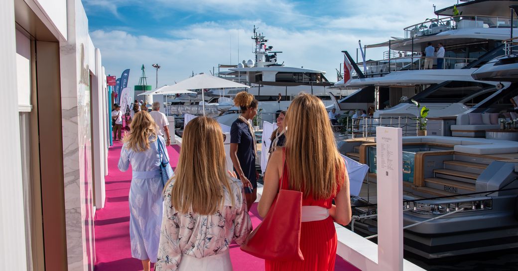 Group of femal visitors walking along a red carpet by some superyachts at the Monaco Yacht Show