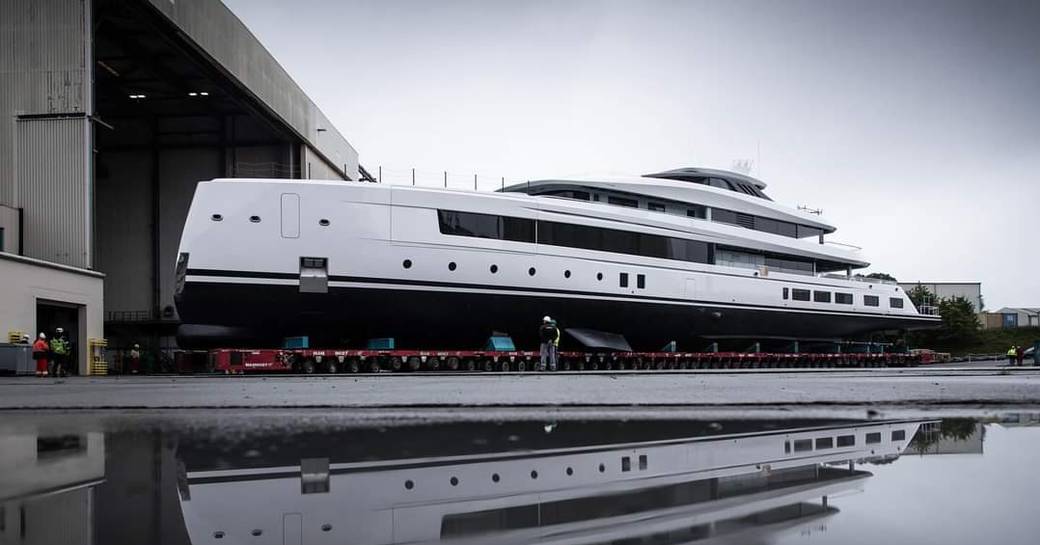 Long side image of superyacht CALI being escorted out of her construction shed