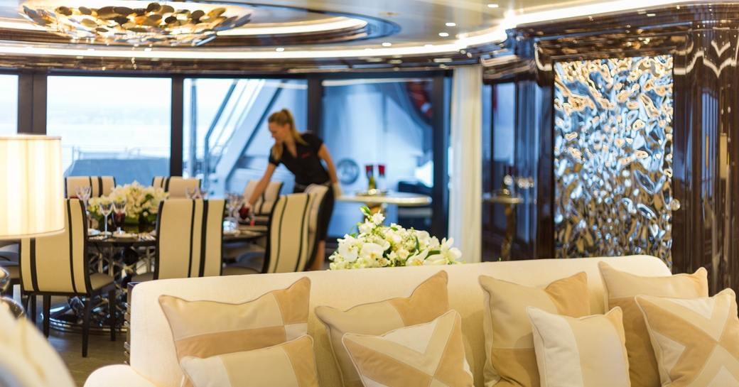 stewardess arranges circular table for dinner in the indoor-outdoor dining area on board superyacht OKTO 