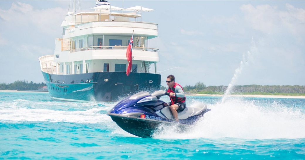 A charter guest enjoys a jetski whilst superyacht PIONEER sits at anchor a short distance away