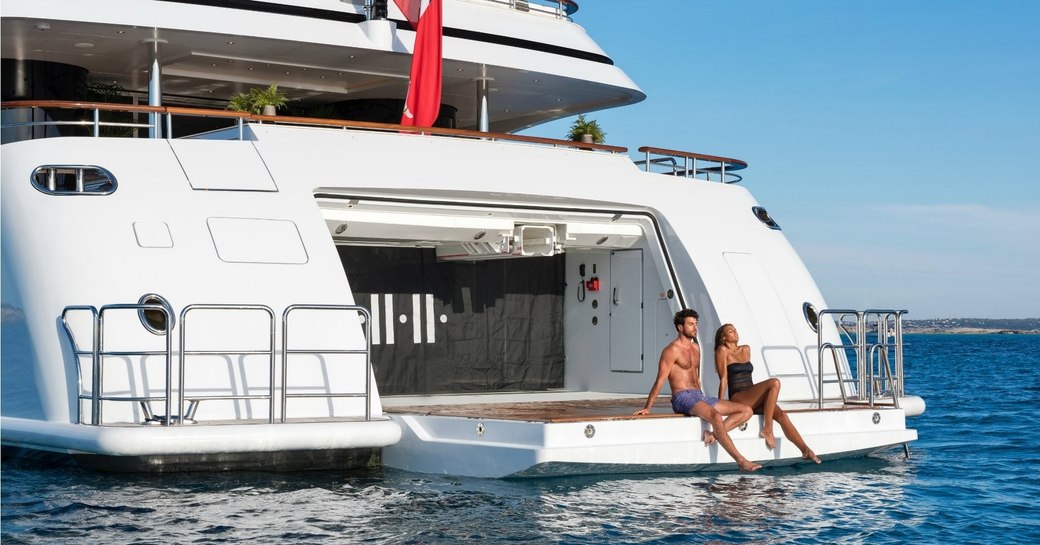 guests sit on the edge of the drop-down swim platform on board superyacht 11/11 