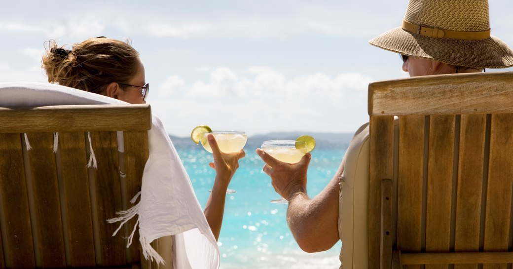 charter guests recline on chaise loungers and enjoy cocktails on beautiful white sand beach