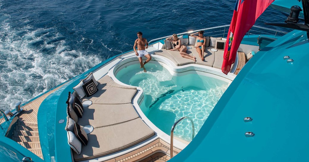 Male and two females relaxing by pool on Superyacht SUNRAYS with sea in background