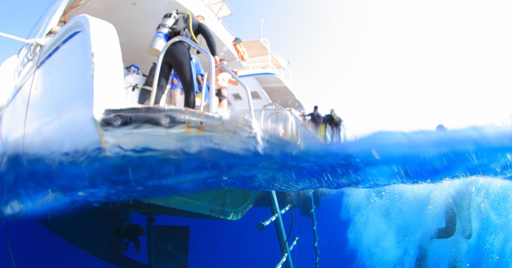 A diver jumps off the back of a charter yacht into blue waters