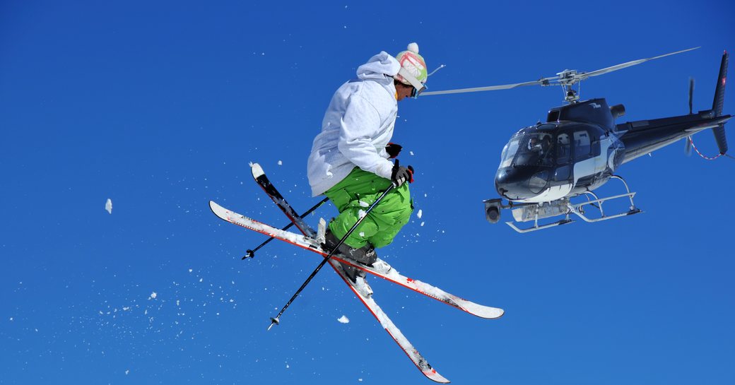 A heliskier jumping with a helicopter mid flight in the background