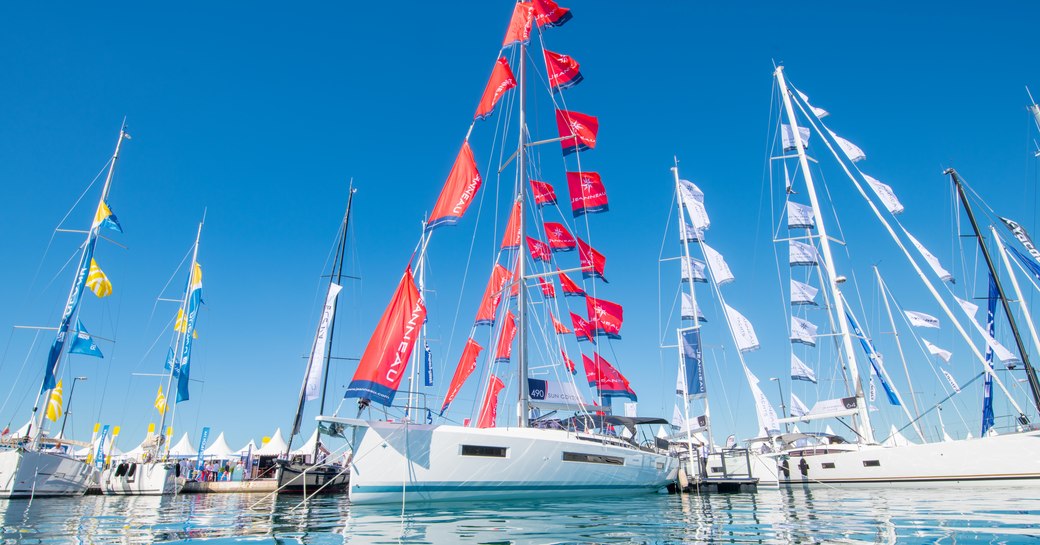 Sailing boats on display with flags at Cannes Yachting Festival, surrounded by sea and clear blue sky.
