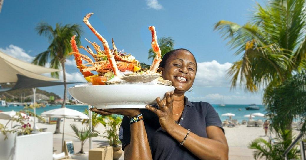 waitress serves huge plate of Caribbean lobster in beautiful beach-side restaurant
