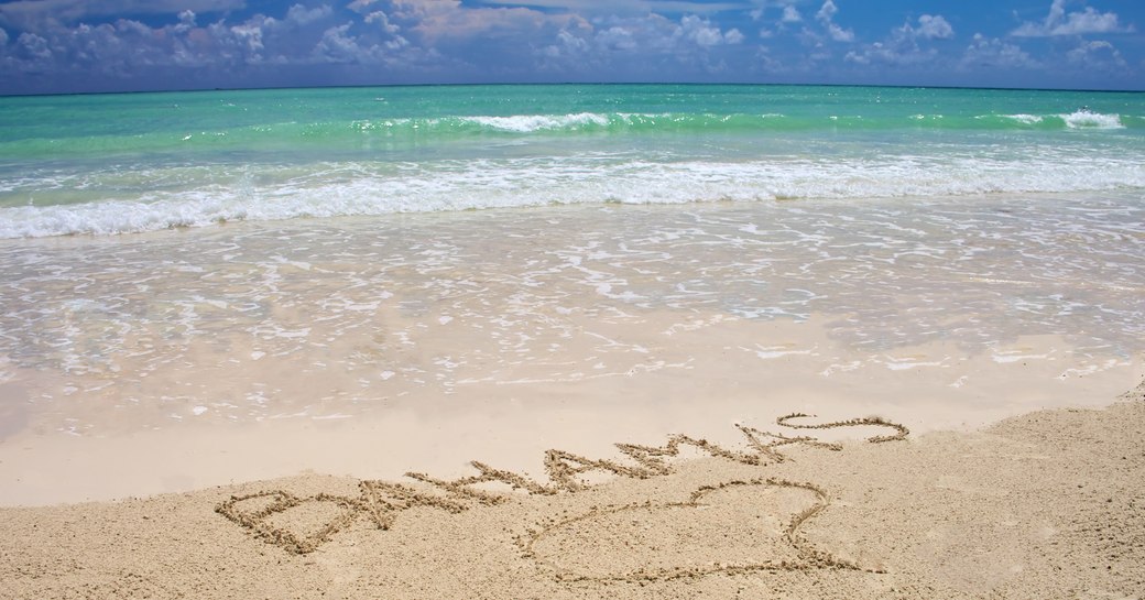 Tropical beach in Bahamas with bright blue sky, turquoise water and writing on the sand