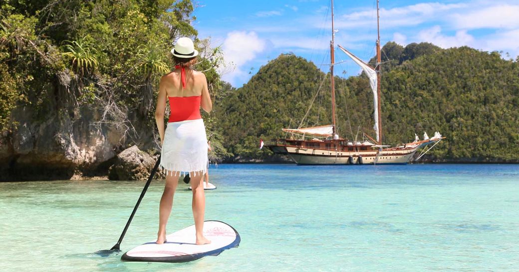 charter guest tries at a paddle board as luxury yacht LAMIMA anchors nearby