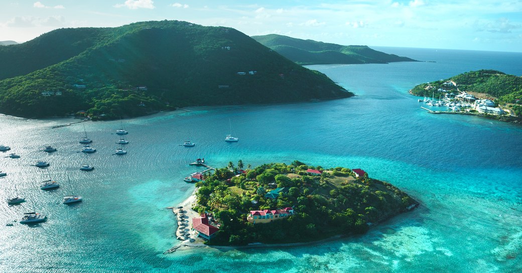 Scattering of green islands with aquamarine lagoons in Virgin Islands in the Caribbean with charter yachts in foreground