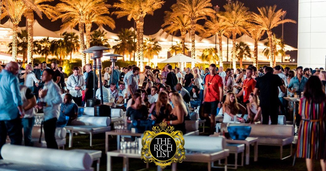 People sitting outside at The Rich List at Palm Island event at Yas Viceroy Hotel with palm trees lit up in background