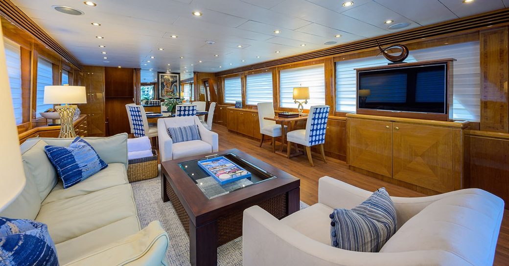 Main salon lounge area onboard charter yacht NEXT CHAPTER, plush white seating surrounds a low coffee table opposite a large retractable TV