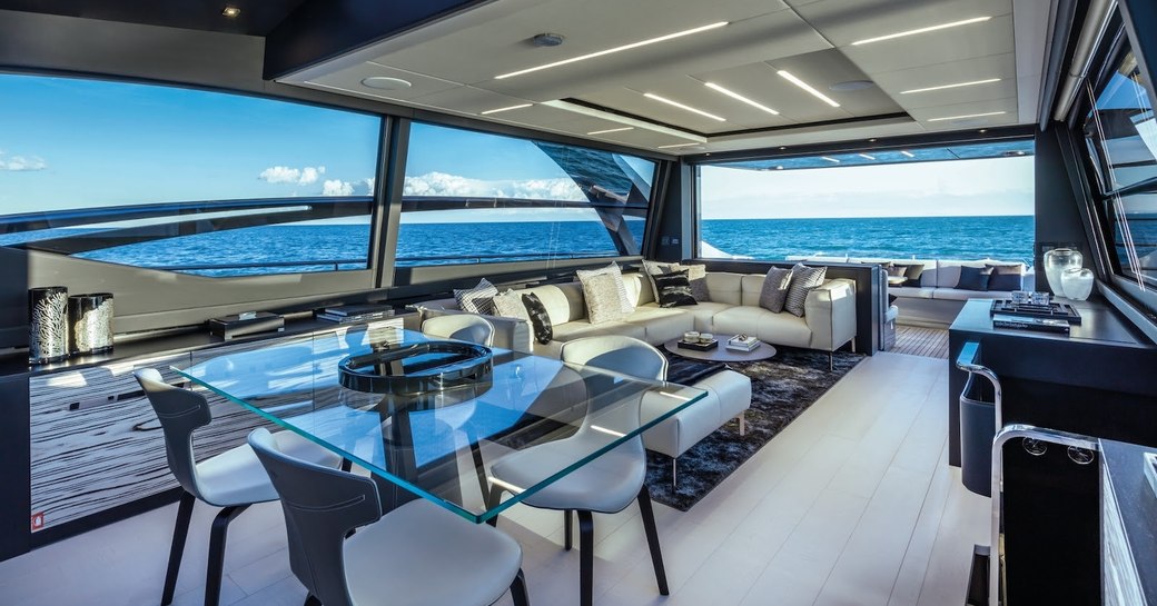 Dining area under cover on motor yacht BEYOND, with tables and chairs and comfortable sofa and sea visible in background.