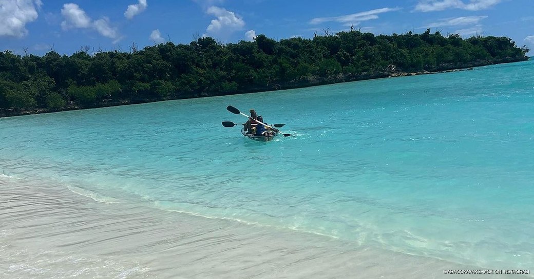 People in a 2-man kayak on the blue water near the shoreline 