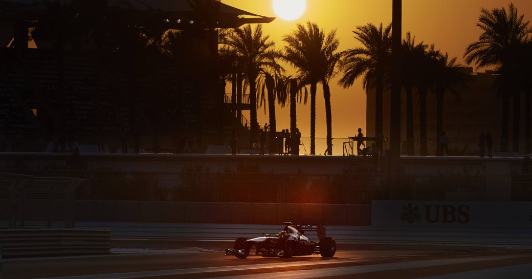 Racer on Abu Dhabi Grand Prix track at sunset, sun setting on background casting shadows over track.