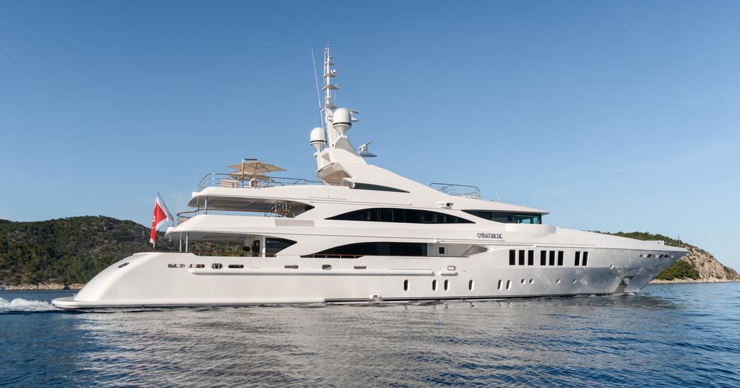 Luxury charter yacht O'MATHILDE underway, surrounded by sea with an island in the background