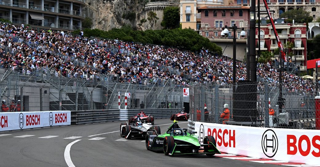 Formula E race in progress, racer in foreground with stands and spectators in background.