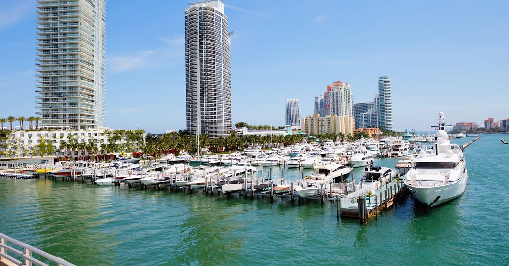 A marina in Miami with many motor yachts berthed against a cosmopolitan backdrop.