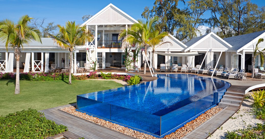 thanda island villa accommodation with infinity pool with glass rim in foreground and suites in background, with palm trees lined up infront